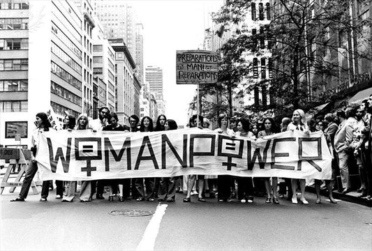 A line of woman hold a white banner with "woman power" written on it in capital letters, 1971