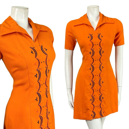 Mannequin wears a bright orange short sleeved mod 60s 70s shirt dress with blue geometric embroidery