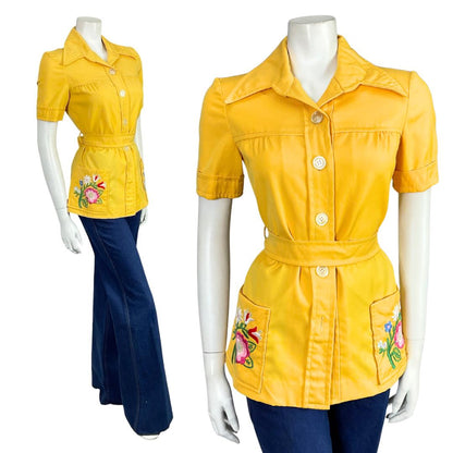 Mannequin wears a bright yellow short sleeve dagger collar 60s 70s mod tie waist shirt with blue flared jeans. 