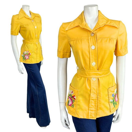 Mannequin wears a bright yellow short sleeve dagger collar 60s 70s mod tie waist shirt with blue flared jeans. 