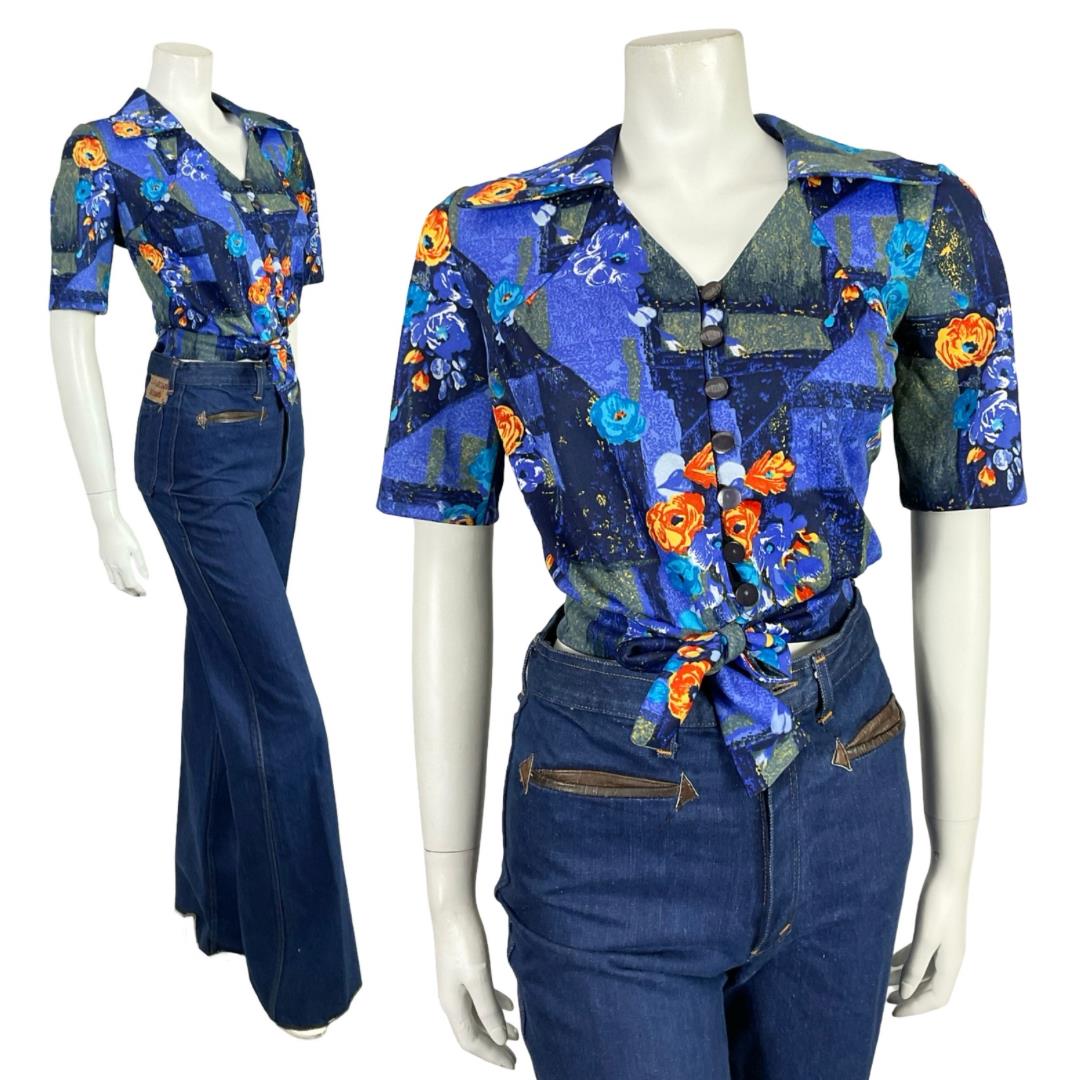 Mannequin wears a blue and orange floral open dagger collar short sleeve tie waist cropped shirt with blue flared jeans. 