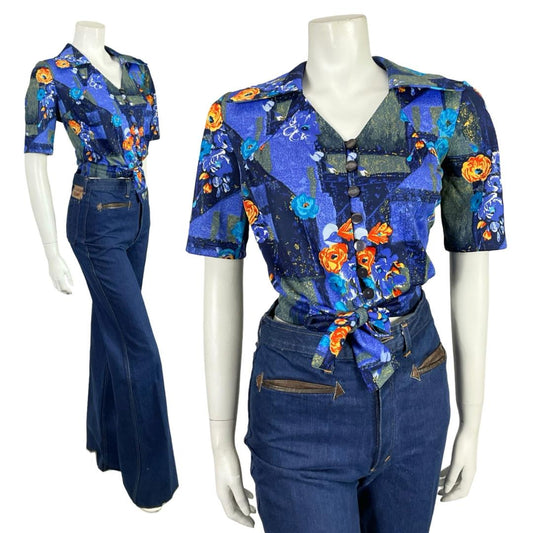 Mannequin wears a blue and orange floral open dagger collar short sleeve tie waist cropped shirt with blue flared jeans. 