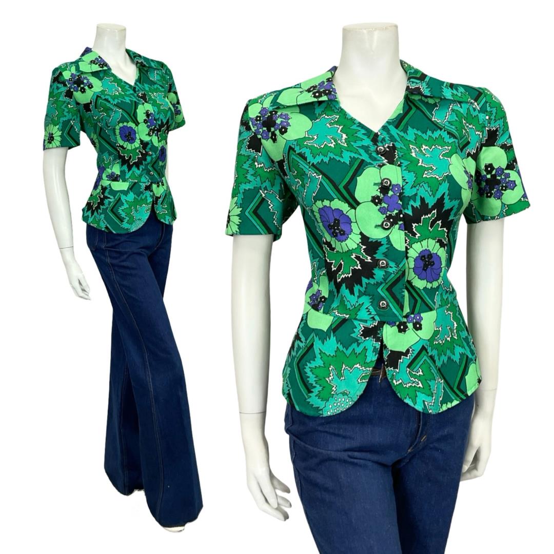 Mannequin wears 60s 70s green and black geometric floral peplum dagger collar shirt with blue flared jeans