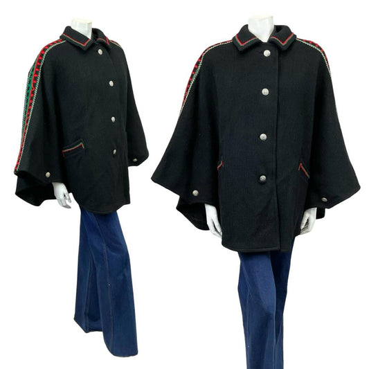 Vintage 60s 70s black collared cape with red and green folk embroidery on a white mannequin wearing blue flared jeans 