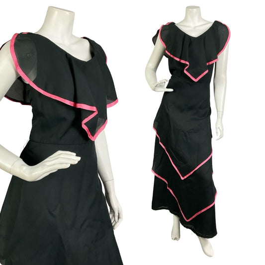 Mannequin wears a black cape tiered floaty maxi dress with a pink trim. 