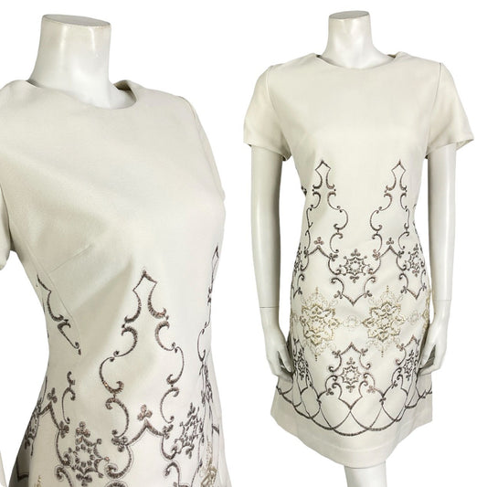 Mannequin wears a white mod shift dress embroidered with a gold and bronze geometric design.