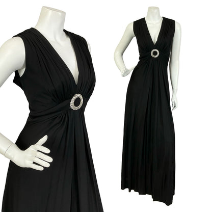 Mannequin wears and all black, ruched, sleeveless maxi dress with an O-ring diamanté decoration in the centre of the waistband. 
