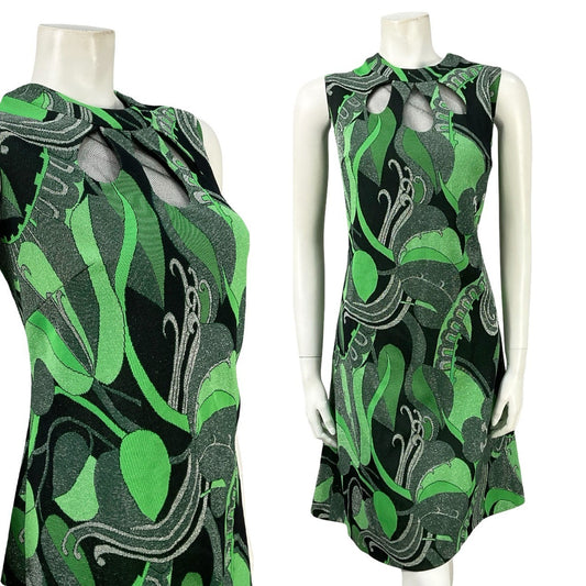 mannequin wears a vintage 60 sleeveless shift dress with teardrop cut outs at the neckline and printed with glittery psychedelic swirls in green, black and silver. 