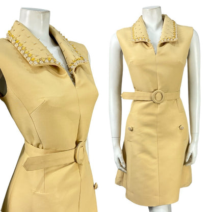 Mannequin wears a beige sleeveless vintage 60s mini dress with a beaded, oversized collar and belt. 