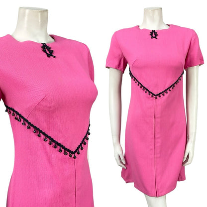 Mannequin wears a vintage 60s mod hot pink, short sleeved shift mini dress with a navy blue beaded trim. 