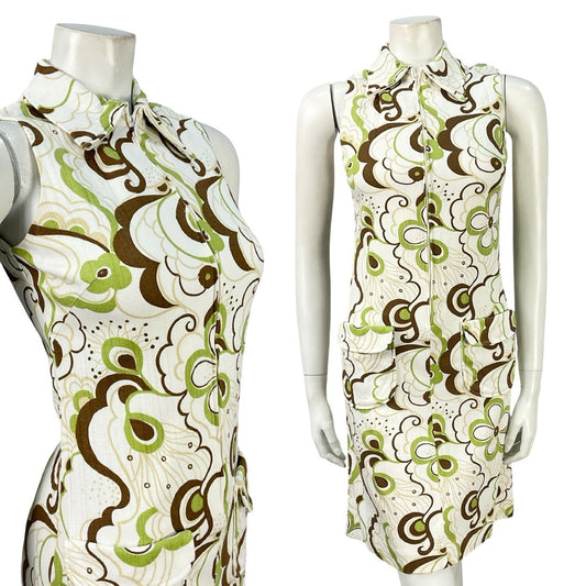Mannequin wears a white, brown and green psychedelic floral dagger collar shirt dress with a body on fit and zip up front. 