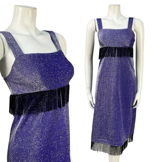 Mannequin wears a purple lurex strappy midi empire line dress with black fringe at the waistline and hemline. 
