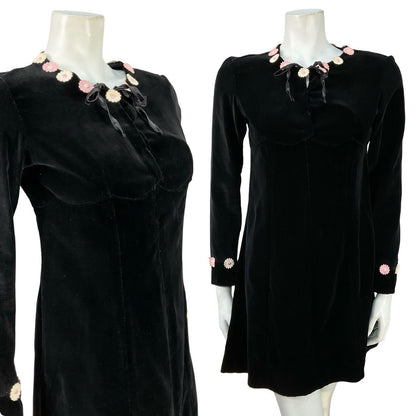 Mannequin wears a black velvet vintage handmade long sleeve shift dress with pink and white flower embellishments on the neckline. 