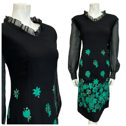 Mannequin wears a black and green floral embroidered shift dress with mesh sleeves and a ruffled neckline.