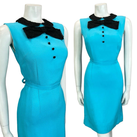 Mannequin wears a vintage 60s mod style bright blue sleeveless mini dress, with a contrast black bow and peter pan collar. The dress also can be tied around the waist with a matching blue fabric tie